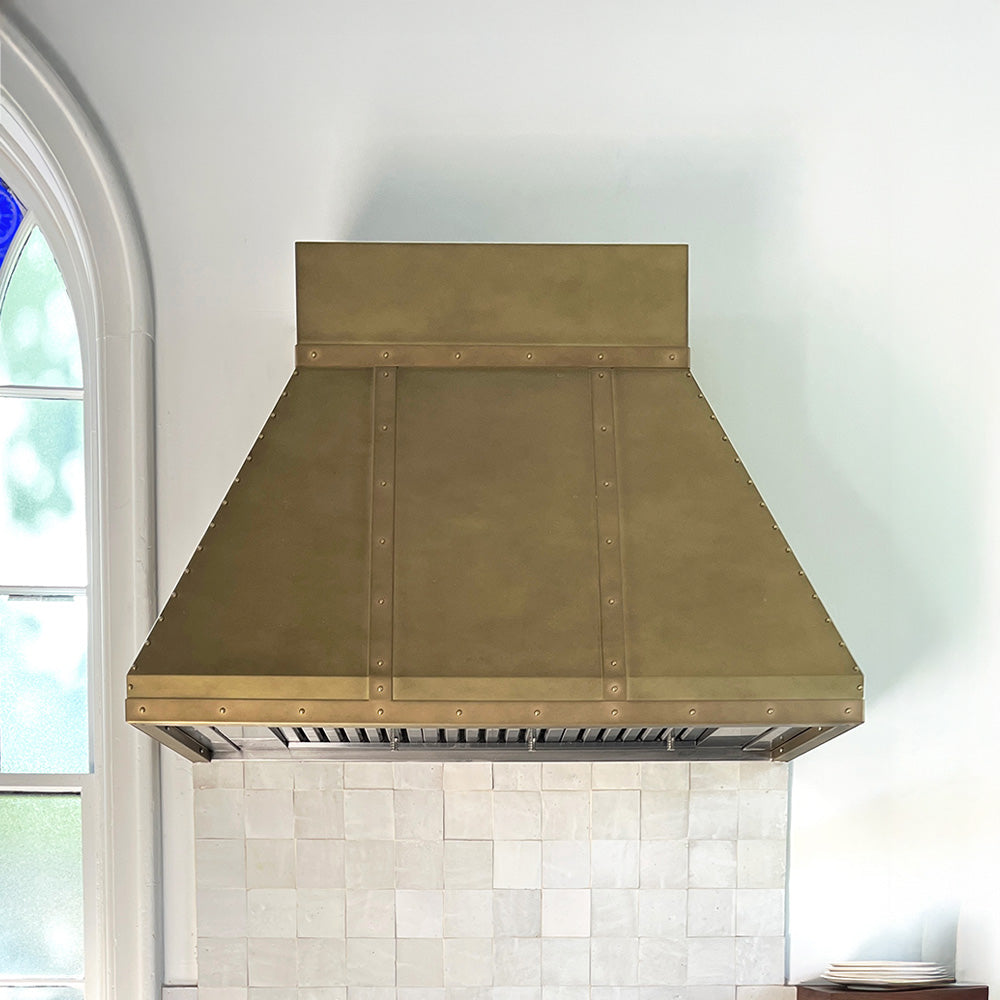 antique brass range hood installed in a rustic white kitchen