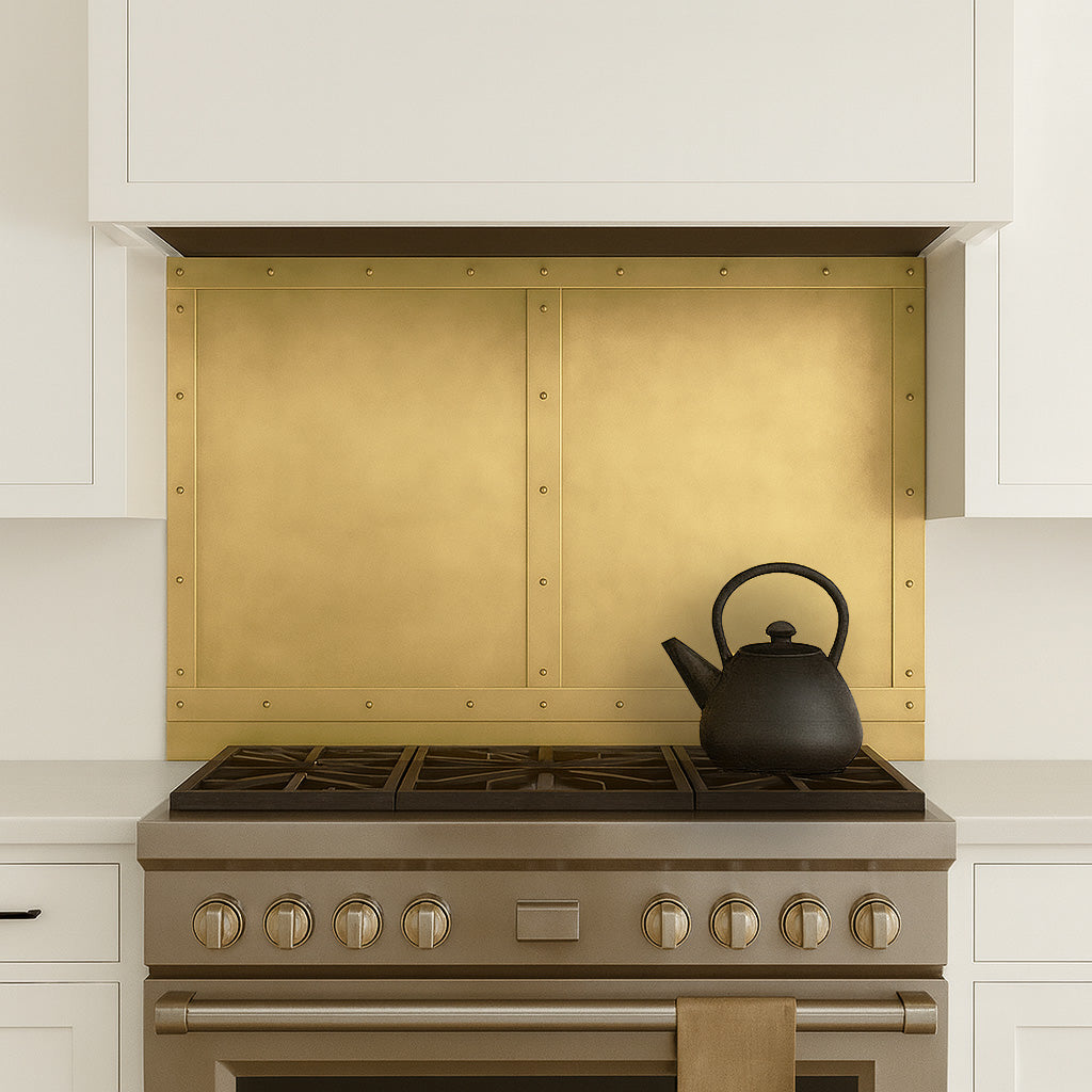 Custom brass kitchen backsplash panel behind cooktop and range hood